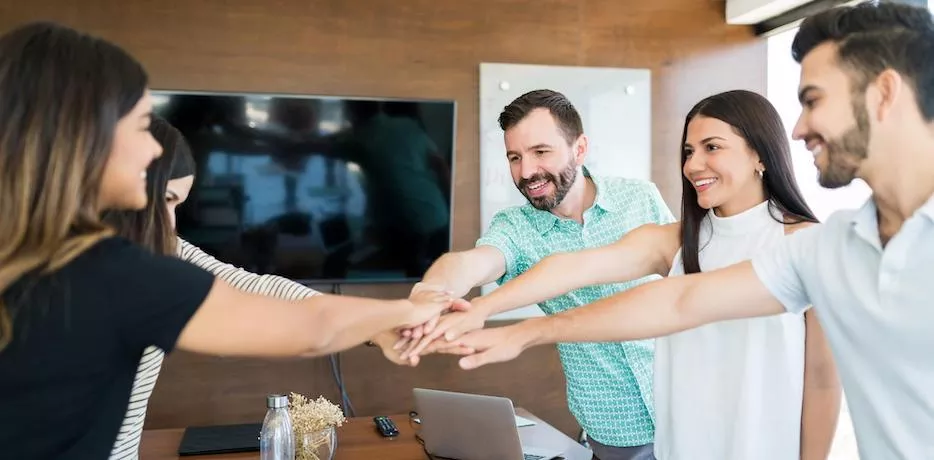 Equipo de trabajo colaborando con entusiasmo en una reunión, simbolizando beneficios laborales y salario emocional en empresas modernas 
