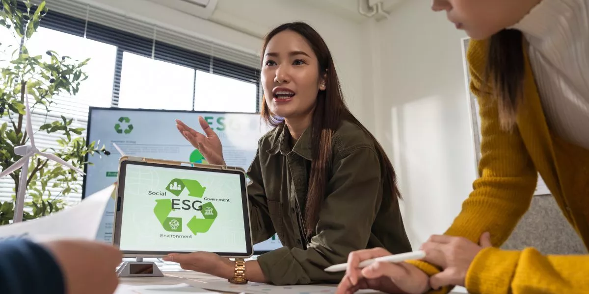 Profesional mostrando en una tablet una presentación sobre pilares ESG durante una reunión laboral, mientras explica estrategias de sostenibilidad al equipo.