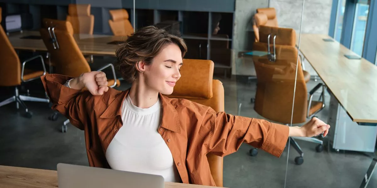 Mujer estirándose en una oficina moderna, representando bienestar laboral y equilibrio en el trabajo.