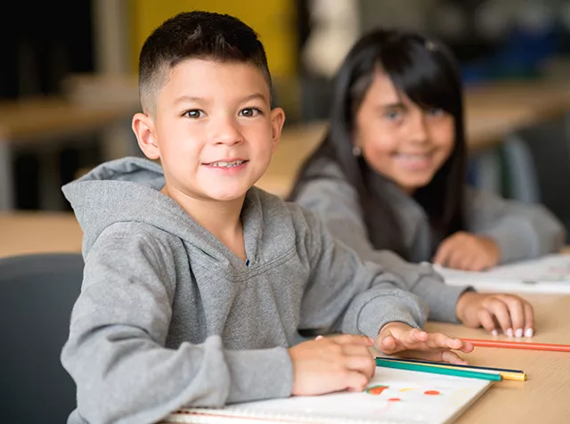 La foto muestra a un niño sonriendo durante una clase en la escuela, reflejando un ambiente de aprendizaje positivo.