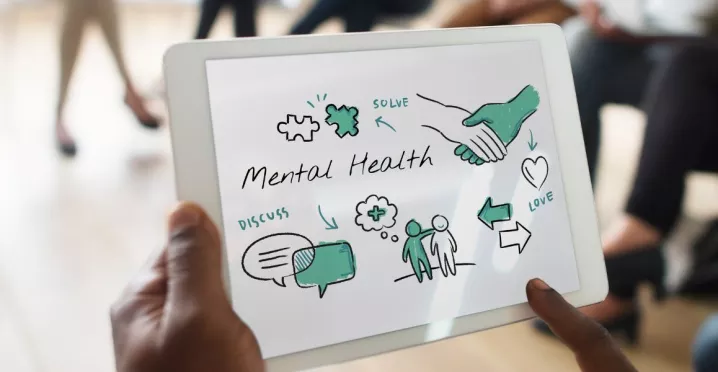 Hombre sostiene tablet con esquema de bienestar y salud mental en reunión de trabajo