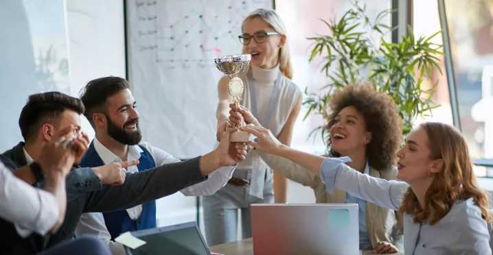 Equipo de trabajo celebrando un logro y sosteniendo un trofeo en señal de reconocimiento laboral.