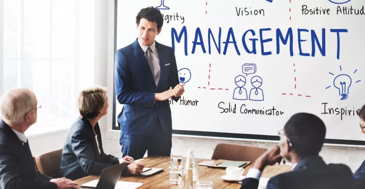 Presentación de un líder frente a un equipo en una sala de reuniones, con una pizarra que muestra conceptos de gestión y liderazgo