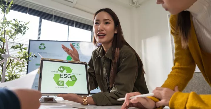 Profesional mostrando en una tablet una presentación sobre pilares ESG durante una reunión laboral, mientras explica estrategias de sostenibilidad al equipo.