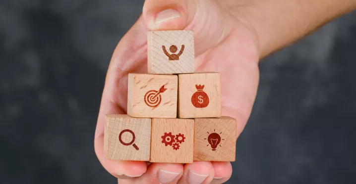 Mano sosteniendo bloques de madera en forma de pirámide con íconos que representan beneficios laborales peru