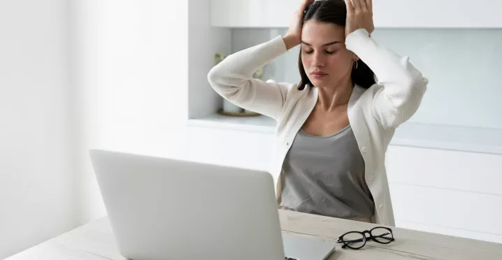Mujer con dolor de cabeza mientras trabaja en la laptop debido al sindrome burnout