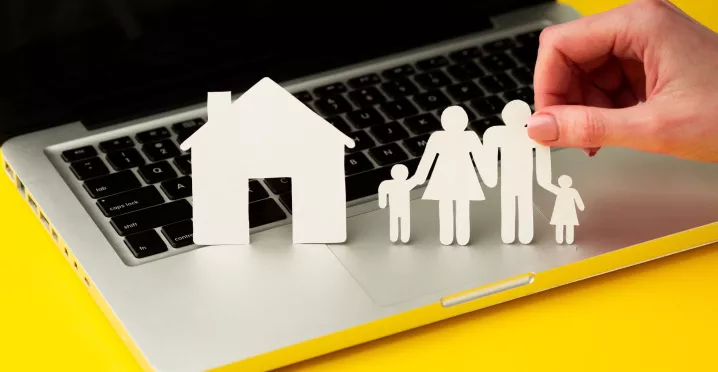 Figuras de papel de una familia y una casa sobre una computadora, en representación de la conciliación laboral y familiar.