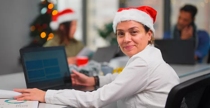 Una mujer feliz trabajando con un gorro de Navidad puesto.
