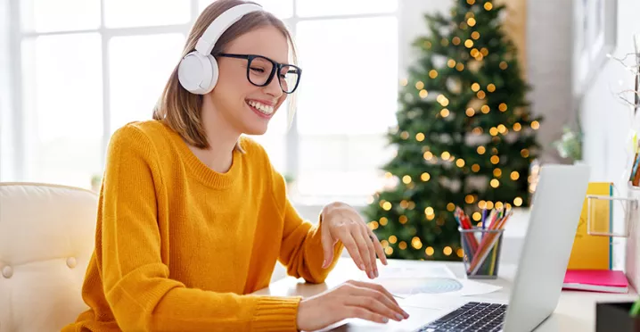 Mujer usando auriculares mientras sonríe, con un árbol de Navidad de fondo.