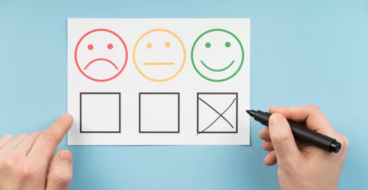 Persona marca la opción positiva en una encuesta de satisfacción laboral con caras que representan distintos niveles de satisfacción.