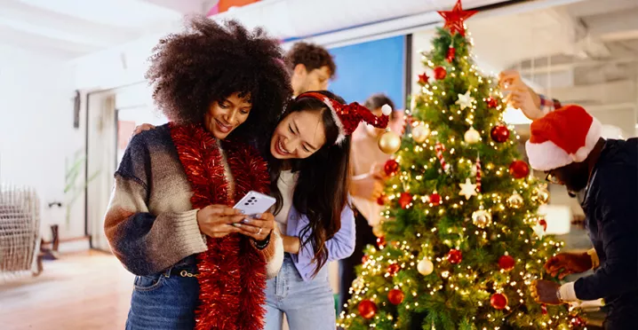 Dos compañeras de trabajo miran el celular durante la fiesta navideña de la empresa.