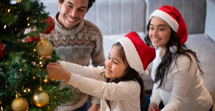 Niña decora el árbol de Navidad de su casa junto a su familia.