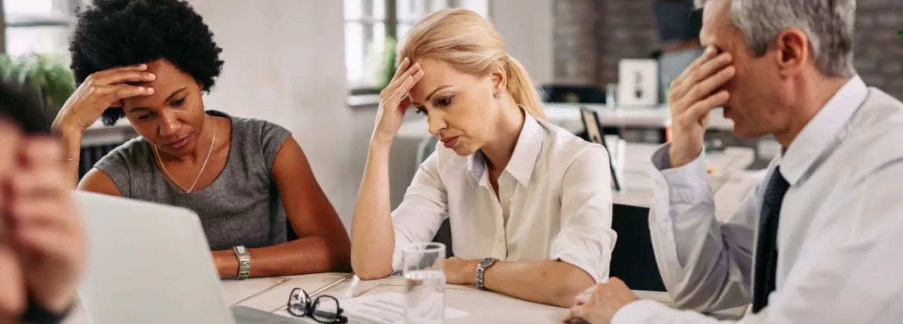 Equipo de trabajo en una reunión muestran signos de preocupación y cansancio frente a una computadora, reflejando desmotivación y bajo rendimiento laboral.