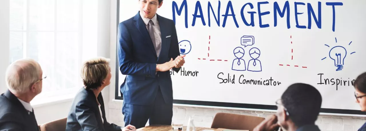 Presentación de un líder frente a un equipo en una sala de reuniones, con una pizarra que muestra conceptos de gestión y liderazgo