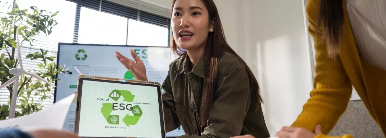 Profesional mostrando en una tablet una presentación sobre pilares ESG durante una reunión laboral, mientras explica estrategias de sostenibilidad al equipo.