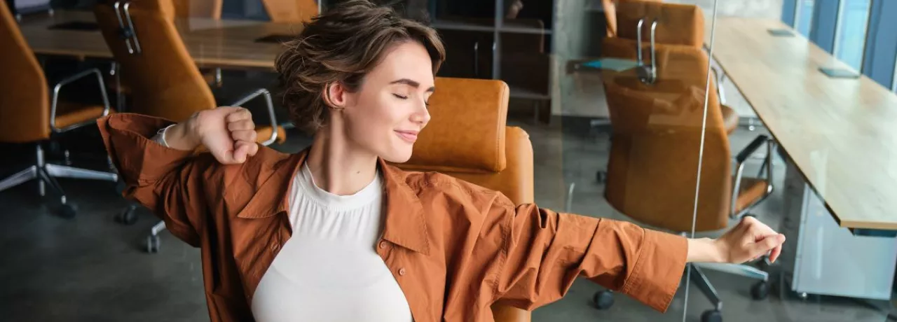 Mujer estirándose en una oficina moderna, representando bienestar laboral y equilibrio en el trabajo.