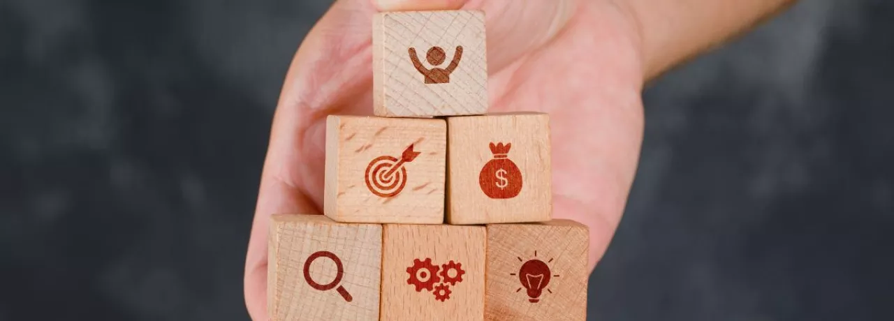 Mano sosteniendo bloques de madera en forma de pirámide con íconos que representan beneficios laborales peru