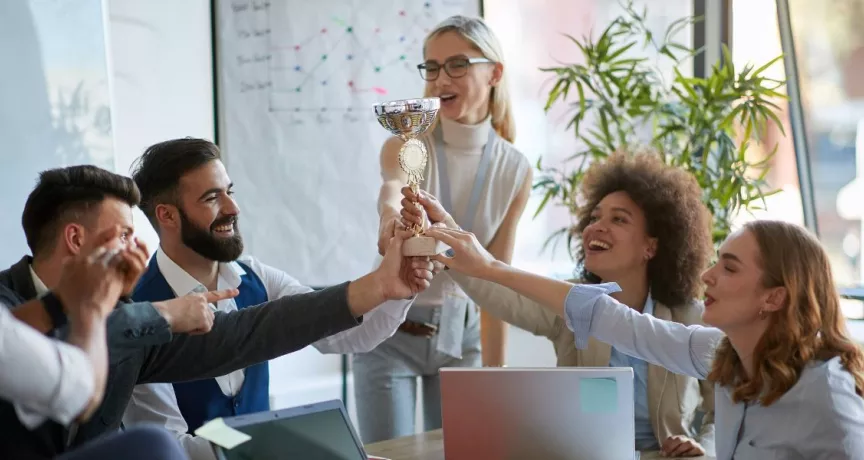 Equipo de trabajo celebrando un logro y sosteniendo un trofeo en señal de reconocimiento laboral.