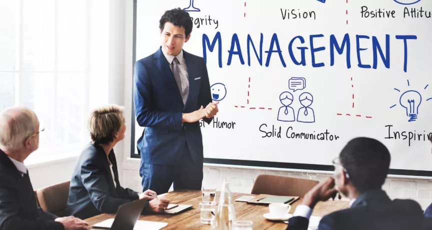 Presentación de un líder frente a un equipo en una sala de reuniones, con una pizarra que muestra conceptos de gestión y liderazgo