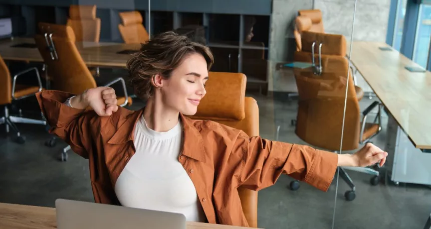 Mujer estirándose en una oficina moderna, representando bienestar laboral y equilibrio en el trabajo.