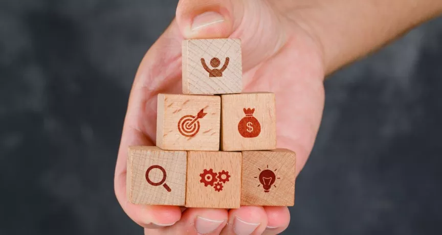 Mano sosteniendo bloques de madera en forma de pirámide con íconos que representan beneficios laborales peru