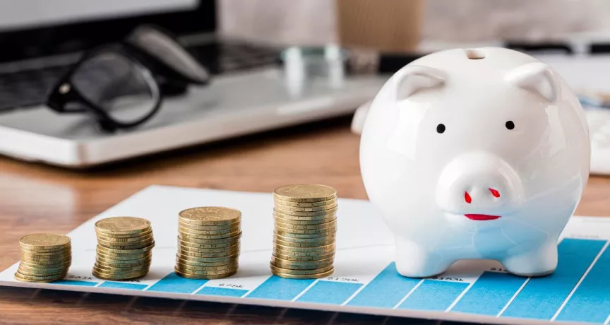 Alcancía junto a pilas de monedas sobre un escritorio, representando ahorro, retorno de inversión y optimización de costos laborales en empresas de Perú.