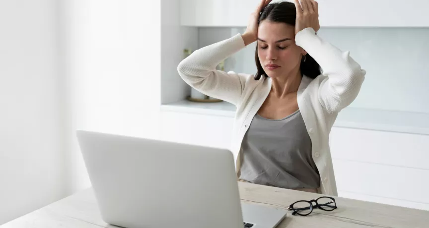 Mujer con dolor de cabeza mientras trabaja en la laptop debido al sindrome burnout