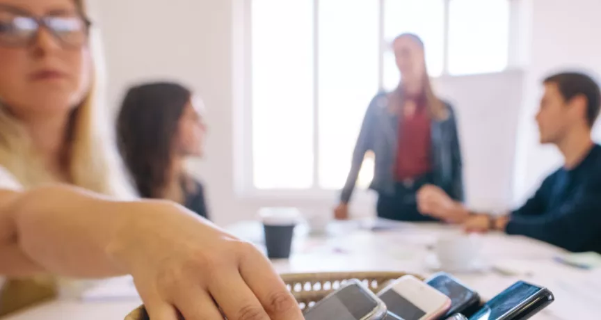 Personas dejando sus celulares sobre una mesa durante una reunión para promover el detox digital y el bienestar digital en el trabajo.