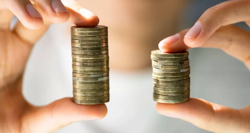 Manos comparan dos pilas de monedas que representan un aumento de sueldo y el crecimiento de la compensación de los colaboradores.