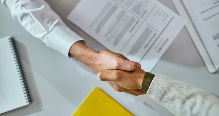 Dos personas se dan la mano sobre un escritorio con documentos al finalizar un proceso de offboarding.
