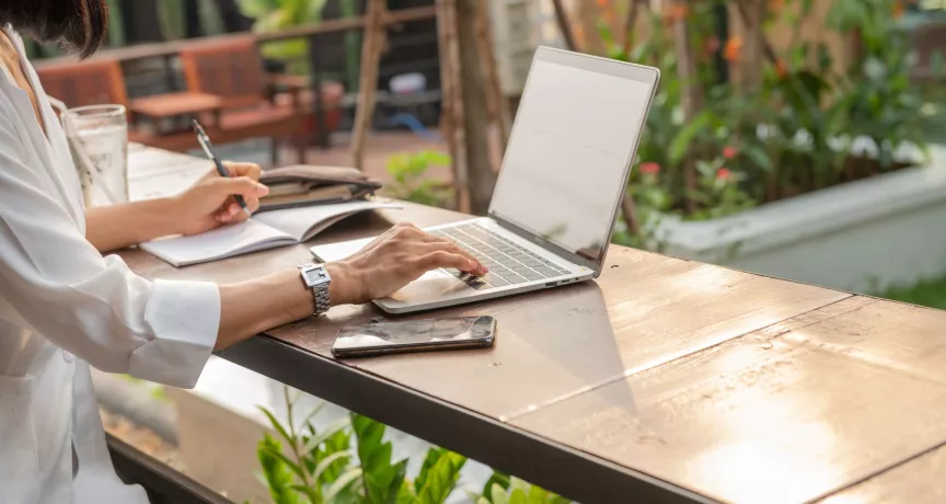 Mujer trabajando de forma remota desde una laptop en un espacio al aire libre.