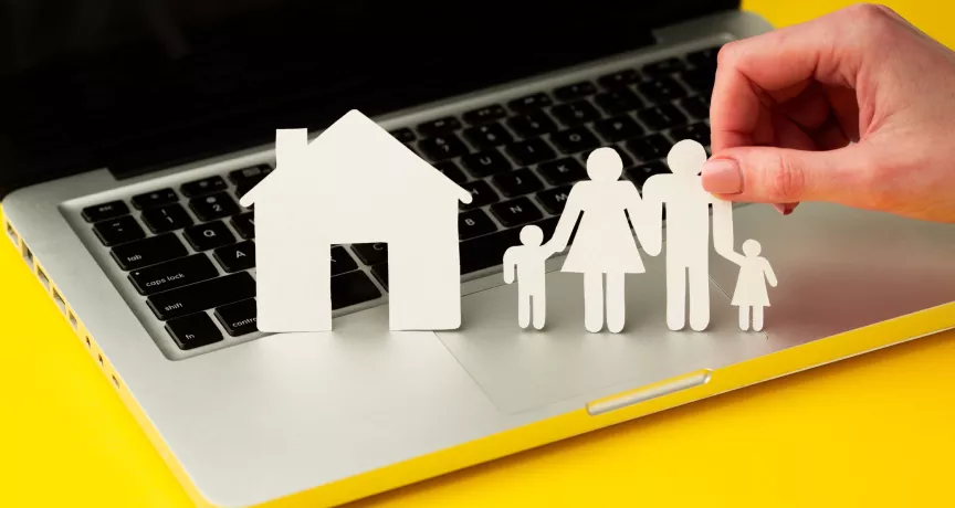Figuras de papel de una familia y una casa sobre una computadora, en representación de la conciliación laboral y familiar.