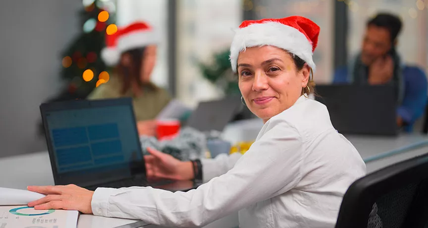 Una mujer feliz trabajando con un gorro de Navidad puesto.