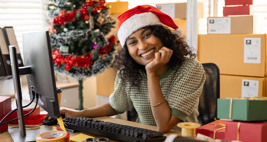 Una mujer con gorro navideño sonríe mientras trabaja.