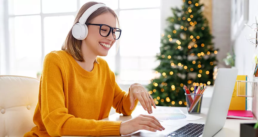 Mujer usando auriculares mientras sonríe, con un árbol de Navidad de fondo.