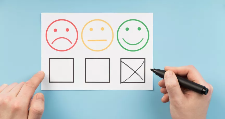 Persona marca la opción positiva en una encuesta de satisfacción laboral con caras que representan distintos niveles de satisfacción.