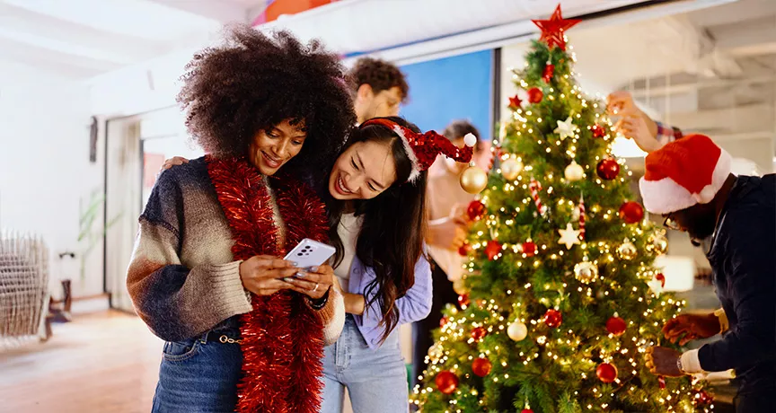 Dos compañeras de trabajo miran el celular durante la fiesta navideña de la empresa.