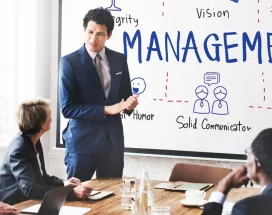 Presentación de un líder frente a un equipo en una sala de reuniones, con una pizarra que muestra conceptos de gestión y liderazgo