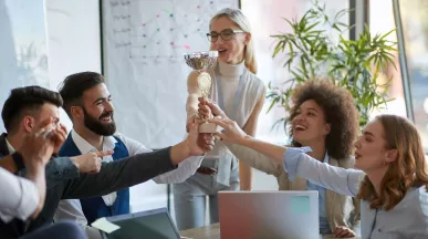 Equipo de trabajo celebrando un logro y sosteniendo un trofeo en señal de reconocimiento laboral.