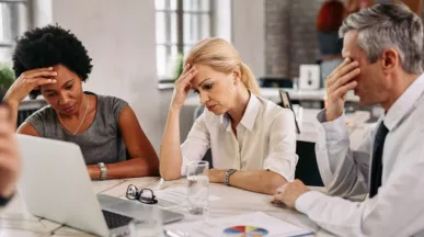 Equipo de trabajo en una reunión muestran signos de preocupación y cansancio frente a una computadora, reflejando desmotivación y bajo rendimiento laboral.