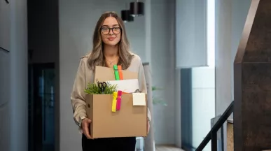 Mujer saliendo de una oficina con una caja de pertenencias tras presentar una renuncia voluntaria de trabajo.