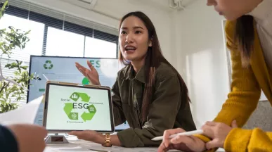 Profesional mostrando en una tablet una presentación sobre pilares ESG durante una reunión laboral, mientras explica estrategias de sostenibilidad al equipo.