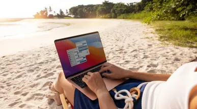 Persona trabajando en una laptop desde la playa durante sus vacaciones, reflejando la dificultad de desconexión laboral en Perú.