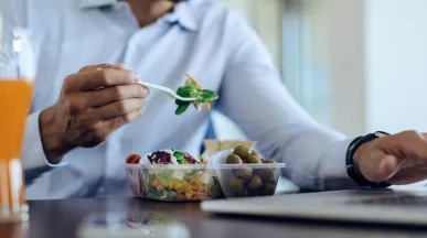 Profesional comiendo alimentos saludables mientras trabaja en la oficina, ejemplo de alimentación y hábitos saludables en el trabajo