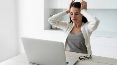 Mujer con dolor de cabeza mientras trabaja en la laptop debido al sindrome burnout