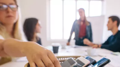 Personas dejando sus celulares sobre una mesa durante una reunión para promover el detox digital y el bienestar digital en el trabajo.