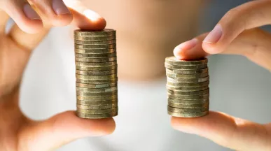 Manos comparan dos pilas de monedas que representan un aumento de sueldo y el crecimiento de la compensación de los colaboradores.