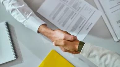 Dos personas se dan la mano sobre un escritorio con documentos al finalizar un proceso de offboarding.
