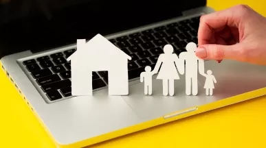 Figuras de papel de una familia y una casa sobre una computadora, en representación de la conciliación laboral y familiar.