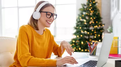 Mujer usando auriculares mientras sonríe, con un árbol de Navidad de fondo.